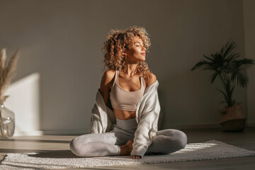Young woman stretching on yoga mat in bright minimal room