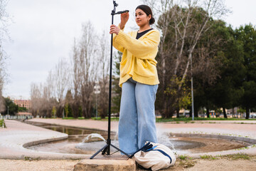 Young woman adjusting her phone on a tripod getting ready to film a video blog in a park