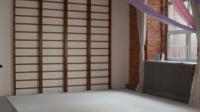 Spacious gym with wall ladder, hammocks for aero yoga, bottles of water on windowsill and white rug on the floor ready for active people or aport lovers