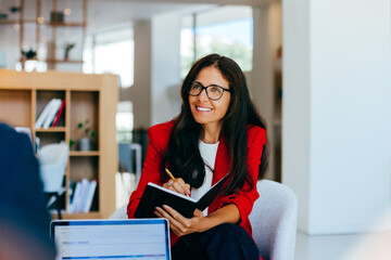 Confident woman in a red blazer taking notes during a business conversation