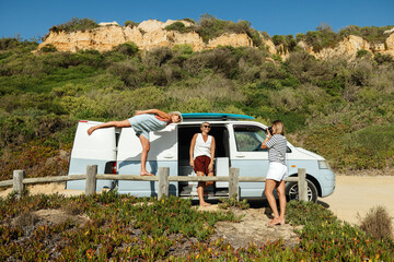 Surfer posing playfully near camper van with scenic cliffs in the background