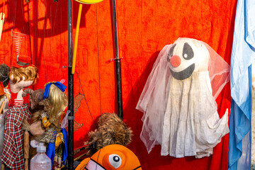 Colorful theater scene with puppets and props against a vivid red fabric backdrop. A clown puppet...