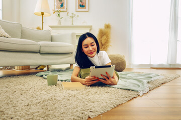 Beautiful long hair Asian woman living free life lying carpet playing tablet with both legs...