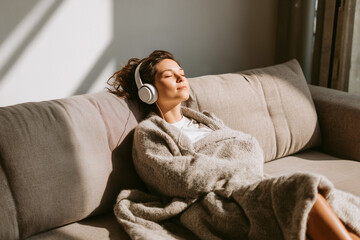 Young woman relaxing with headphones on beige sofa in natural light