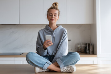 Young woman using smartphone while sitting on kitchen counter