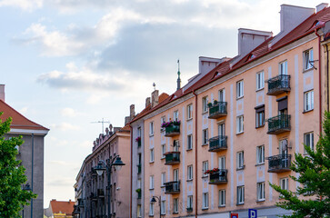 Fototapeta premium Row of residential buildings with red gable roofs and balconies decorated with flowers. Classic post-war urban architecture under a partly cloudy sky.