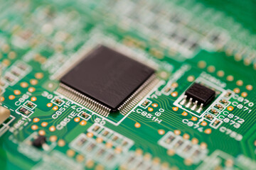 Macro view of a black microchip with fine pins mounted on a green printed circuit board. 