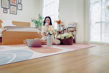 Asian woman spending her free time at home on her holiday in her bedroom enjoying arranging pastel colored plastic roses in a vase to decorate her home beautifully.