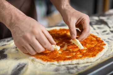 Close up picture of cookers hands putting topping o the pizza