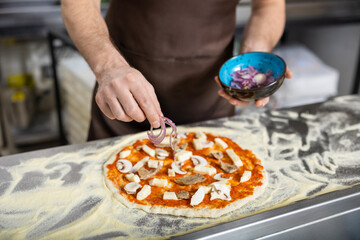 Close up picture of cookers hands putting topping o the pizza