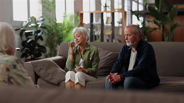 Elderly husband and wife sitting on sofa, talking about their issues and expressing emotions to a therapist in a mental health support session