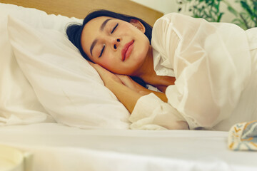 Asian woman taking nap during the day relaxing during the holiday at home dreaming and wanting to wake up late on a comfortable bed in a bedroom with air conditioning that makes her sleep better.