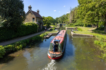 Canal barge being steered slowly through Walsham Gates Lock on the River Wey Navigation, while...