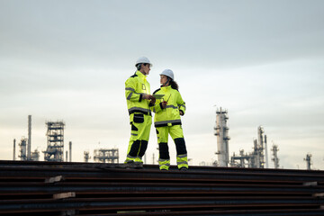Engineer worker watching work monitor on digital tablet and checking for quality control at construction site of petroleum chemical industry or refinery oil plant factory overtime at night