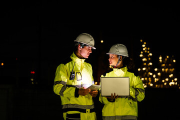 Engineer worker watching work monitor on laptop and checking for quality control at construction site of petroleum chemical industry or refinery oil plant factory overtime at night