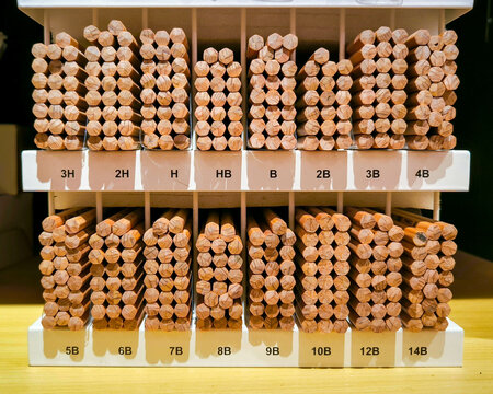 Organized stacks of various-grade wooden pencils neatly displayed in a store rack, showing labeled hardness marks&mdash;ideal visual for education supplies and art tools.