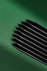 Several black pens are neatly aligned on a green surface, creating a visually appealing contrast....