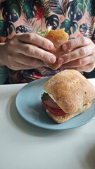 A person holding a fresh ciabatta sandwich filled with vegetables and meat.