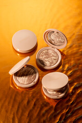 Four makeup compacts are artistically arranged on a shimmering golden surface, highlighting intricate marbled patterns and soft hues under warm lighting.