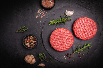 Raw steak burgers patties with ground beef and spices on a cutting board. Dark background, top view.
