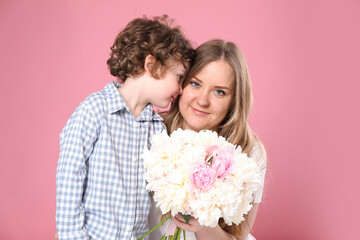 Little boy giving his mom beautiful peony flowers on pink background