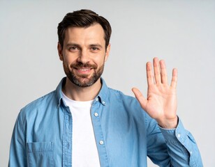 Fototapeta premium A friendly bearded man in a casual blue shirt smiles warmly and waves with an open hand, exuding a welcoming and positive demeanor against a neutral background.
