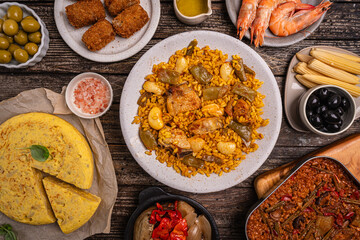 Spanish food table paella valenciana, croquettes, omelette, and tapas slices jamon, bowls with olives, spicy potatoes, shrimp. Typical spanish dishes, tapas set concept. Variety of plates