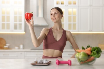 Woman holding bell pepper near table with kitchen scale, measuring tape, dumbbells and healthy food...