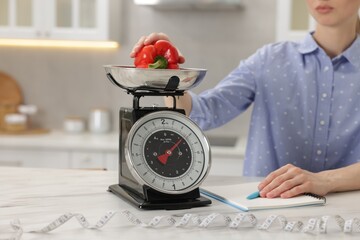 Woman weighting bell pepper on kitchen scale at white marble table indoors, closeup