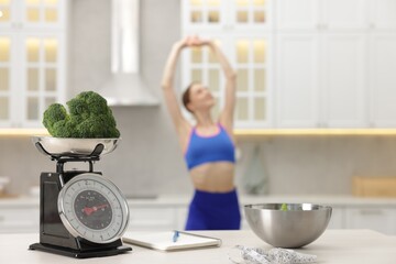 Slim woman posing indoors, focus on kitchen scale, broccoli, notebook, measuring tape and salad