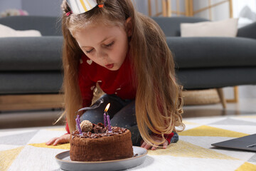 Birthday celebration. Little girl blowing candles on cake while having video call via laptop at home