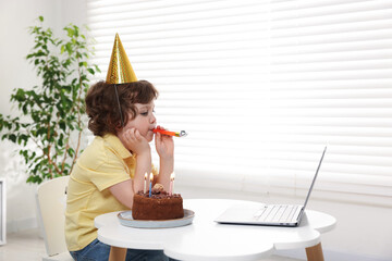 Little boy celebrating his birthday while having video call via laptop at table indoors. Space for...