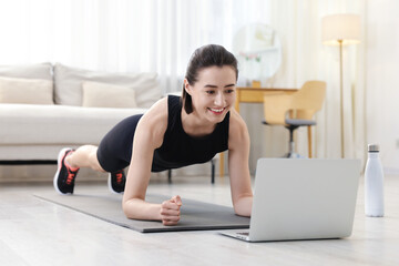 Fototapeta premium Woman doing plank exercise during online class with coach at home. Sport and healthy lifestyle