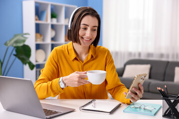 Smiling woman with smartphone and cup of hot drink at desk in home office