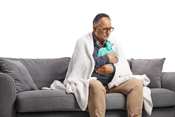 Fototapeta premium Ill mature man wrapped in blanket sitting on a sofa and holding a body warmer