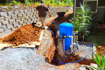 Homeowner works on installing water well pump system near trench in thoughtfully arranged outdoor space.