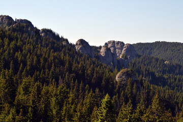 Majestic mountain peaks rise above rolling green hills and pine forests in this scenic landscape of...