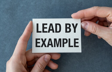 A hand holding a white card that says Lead by Example