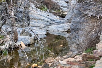  Still water among layered rocks and dry branches in Monfragüe Natural Park, Extremadura, Spain. Peaceful and rugged landscape.
