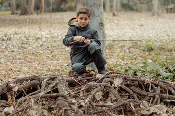 niño jugando en un árbol con raíces con un palo en un día de otoño