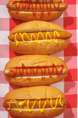 Close-up of four neatly arranged hot dogs with mustard and ketchup on a red checkered background. Tasty fast food concept.