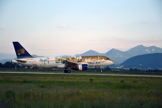 A Nile Air plane lands gracefully at Brașov Airport, Romania, with the scenic Carpathian Mountains in the background. The sunset sky and vivid livery add a dynamic touch to this aviation moment