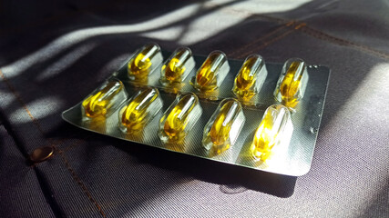 A close-up image of soft gel capsules neatly arranged in a blister pack against a textured fabric background. These dietary supplements, highlight their importance in health and wellness.