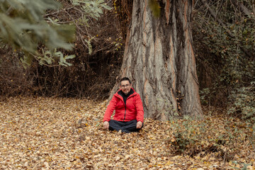 retrato de hombre sentado sobre las hojas caídas en medio del bosque en temporada de otoño