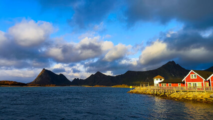 Scenic coastal landscape with mountains, ocean, and a red cabin. Ideal for travel promotions and...