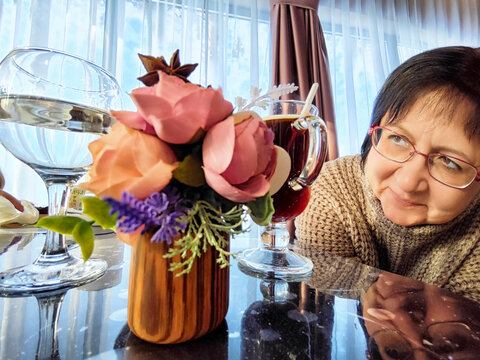 Woman gazes at decorative flowers while beverages rest on the table in a cozy setting during daytime