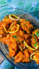 a glass dish filled with vibrant, reddish-orange fried chicken pieces generously coated in a spicy chili sauce