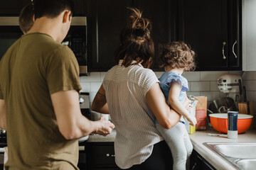 Family baking together in modern kitchen with father cracking egg into bowl and mother holding...