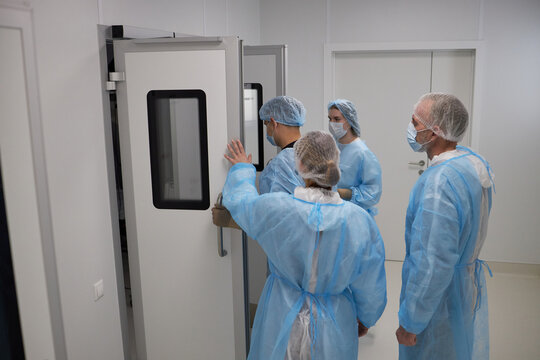 Group of middle aged and senior men and women wearing surgical gowns and masks entering operating room, medical professionals preparing for surgery in sterile environment
