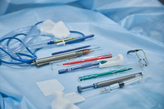 Surgical instruments and medical devices arranged on sterile drape in operating room, including forceps, suction tube, electrosurgical pencil, and disposable scalpels